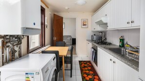Ett kompakt kök med vita skåp, en tvättmaskin från Bosch, en mikrovågsugn och ett handfat.