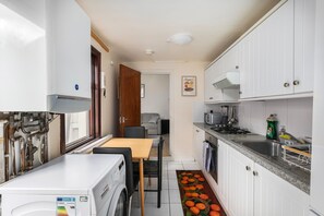 A compact kitchen with white cabinets, a Bosch washing machine, a microwave, and a sink. - Stratford 4-Bed House, Sleeps 8 with Garden (London)