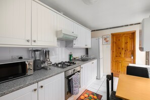 A compact kitchen with white cabinets, a gas stove, a built-in oven, a microwave, and a refrigerator. - Stratford 4-Bed House, Sleeps 8 with Garden (London)