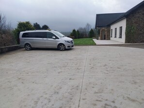 A silver minivan parked in a driveway with a stone building and a lawn in the background. - House Sleeps 11 with Parking (Tralee)