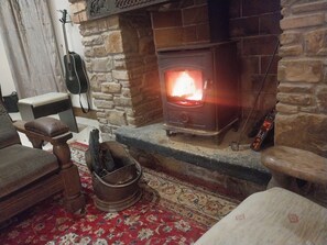 A stone fireplace with a burning fire, a guitar leaning against the wall, and a rustic wooden bench. - House Sleeps 11 with Parking (Tralee)