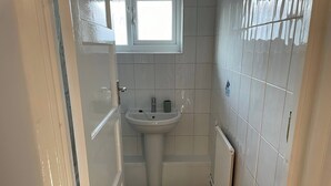 Ein kleines Badezimmer mit einem weißen Waschbecken, einem Fenster und einer Heizung.