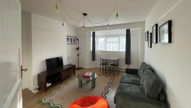 Ein Wohnzimmer mit einer Couch, einem Fernseher, einem kleinen Tisch und einer Stehlampe.