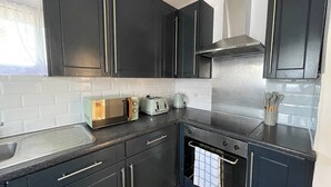 Eine moderne Küche mit dunklen Schränken, einer Edelstahl-Dunstabzugshaube, einem eingebauten Backofen und einer Arbeitsplatte mit Toaster und Wasserkocher.