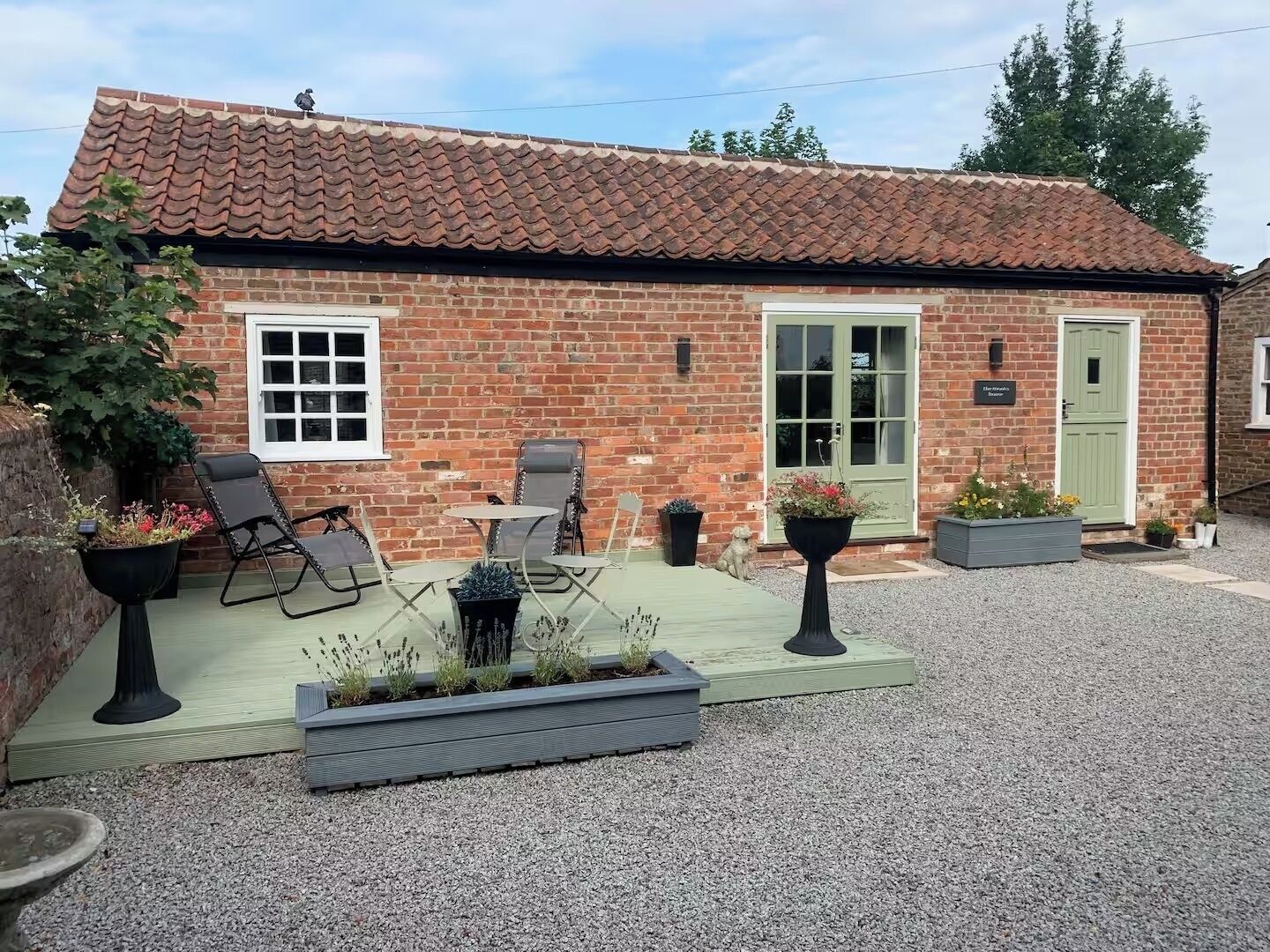 A brick house with a tiled roof, a green door, and a patio area with outdoor furniture and planters.