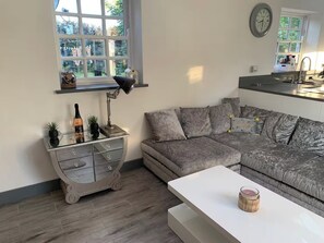 A living room with a grey sofa, a white coffee table, and a glass cabinet with decorative items. - Bungalow Sleeps 2 with Garden (Boston)