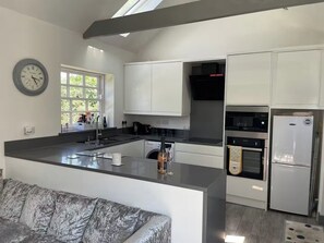 A modern kitchen with white cabinetry, a central island, and a built-in oven. - Bungalow Sleeps 2 with Garden (Boston)