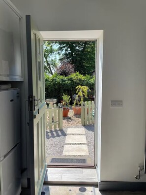 A doorway leading to a garden with a gravel path, potted plants, and a wooden fence. - Bungalow Sleeps 2 with Garden (Boston)