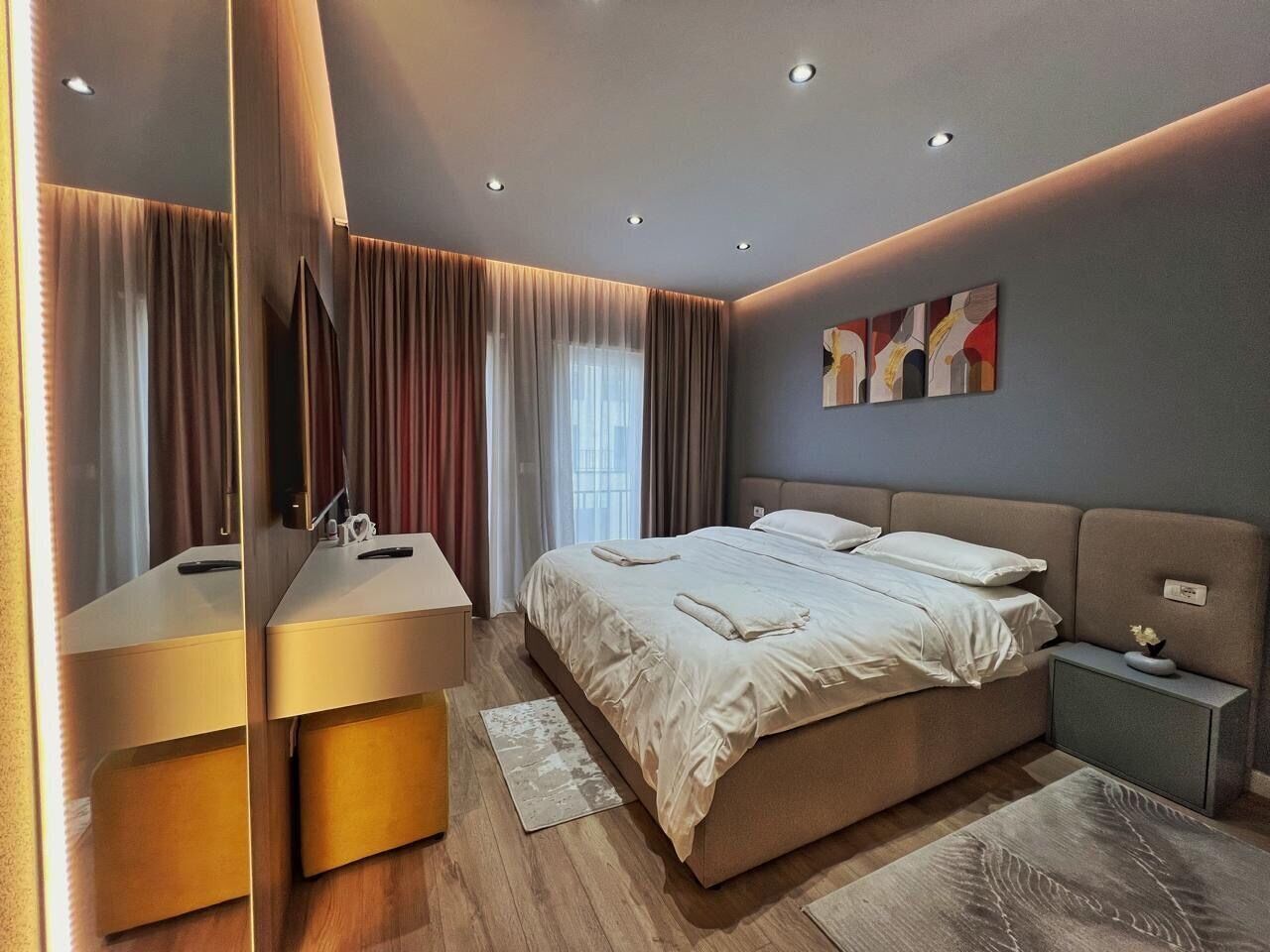 Quarto moderno com cama grande, mesas de cabeceira, um espelho e uma obra de arte pendurada na parede.