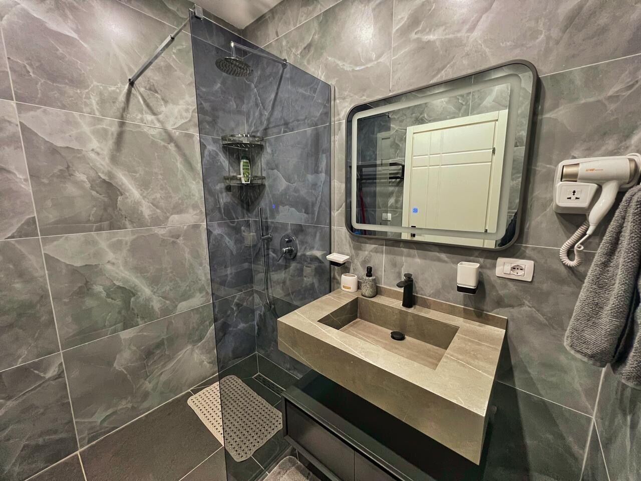 Ein modernes Badezimmer mit einer gläsernen Duschkabine, einem Waschbecken mit Spiegel darüber und einem Handtuch an der Wand.