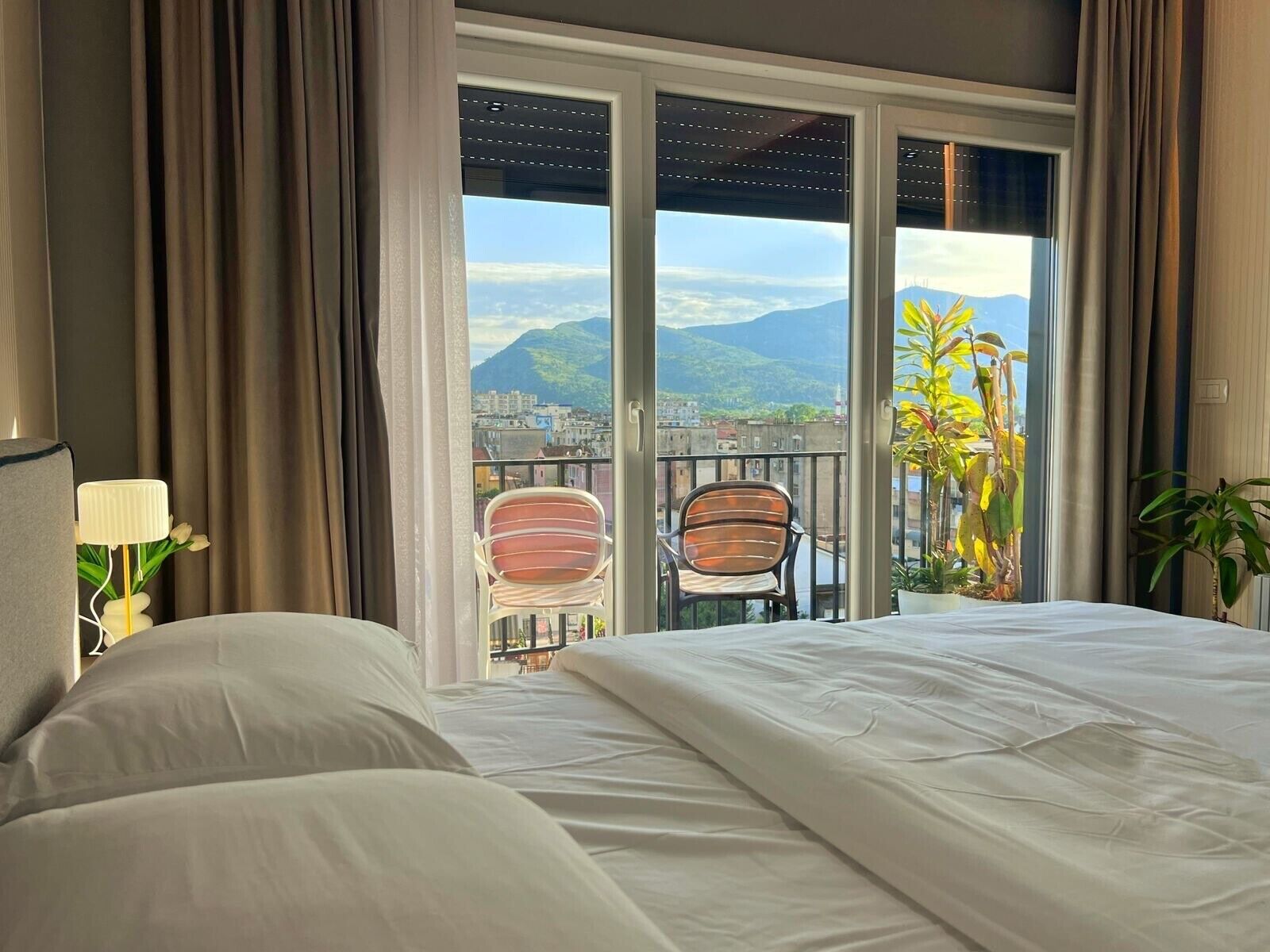 A hotel room with a large bed, a balcony with chairs, and a view of mountains.