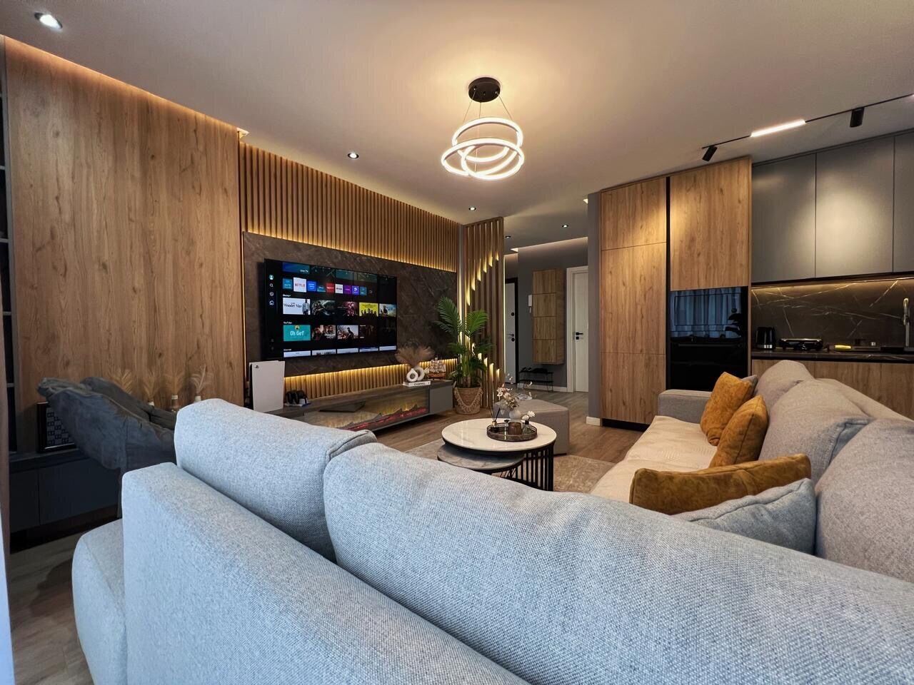Ein modernes Wohnzimmer mit grauem Sofa, Couchtisch und an der Wand montiertem Fernseher.
