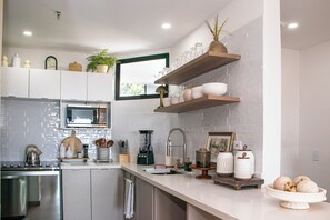 A modern kitchen with white cabinetry, a built-in microwave, and a coffee machine.