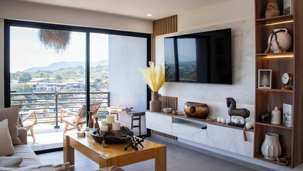 A modern living room with a large TV, a wooden coffee table, a sofa, and a bookshelf with decorative items.