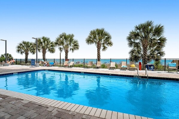 A swimming pool with lounge chairs and palm trees. - Myrtle Beach | Family Oceanfront Getaway | Pool + Beach | 3BR Sleeps 8 (Myrtle Beach)