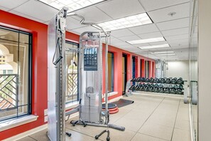 Un gimnasio con equipo de ejercicio, un soporte de mancuernas en la pared y una ventana con vistas a edificios.