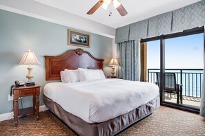 Una habitación de hotel con una cama grande, dos mesitas de noche, un ventilador de techo, un cuadro enmarcado en la pared y un balcón con vistas.
