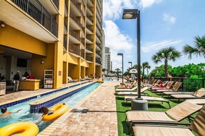A hotel pool area with a swimming pool, lounge chairs, and a building with balconies. - Myrtle Beach | Family Oceanfront Getaway | Pool + Beach | 3BR Sleeps 8 (Myrtle Beach)