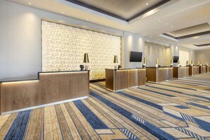 Ein Hotel-Empfangsbereich mit Wandverkleidung, mehreren Empfangstresen und Teppichboden.