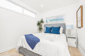 A bedroom with a bed, a nightstand, a lamp, a framed picture, and a plant. - Charming 5BR Group Bungalow Steps to Sand with Deck and Fire Pit (Newport Beach)