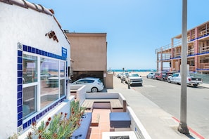 A beachfront property with a parking area, a building with a tiled facade, and a view of the beach. - Charming 5BR Group Bungalow Steps to Sand with Deck and Fire Pit (Newport Beach)