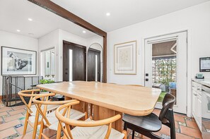 A dining area with a wooden table and chairs, a tiled floor, and a view of the outside. - Charming 5BR Group Bungalow Steps to Sand with Deck and Fire Pit (Newport Beach)