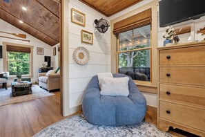 A cozy living room with a blue bean bag chair, wooden cabinets, and a large window with a view of trees. - Crescent Lake 1-Min Walk to Public Beach, Boat Launch, Kayaks, Paddleboards (Raymond)