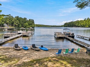 A lakeside dock with boats, a sandy beach, and a row of chairs.