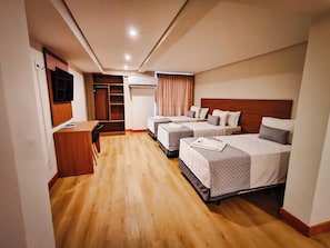 Une chambre d’hôtel avec trois lits, un bureau, une armoire et un téléviseur.