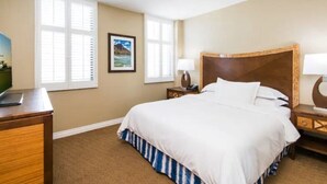 A hotel room with a bed, a desk, a lamp, and a picture on the wall. - Waikiki | Resort Lagoon Stay | Pools & Beach Access (Honolulu)