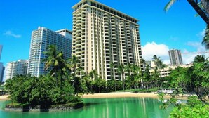 A tall hotel with multiple balconies, surrounded by palm trees and a beach. - Waikiki | Resort Lagoon Stay | Pools & Beach Access (Honolulu)