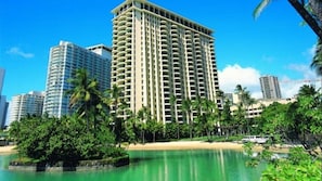 Un hotel alto con varios balcones, rodeado de palmeras y una playa.