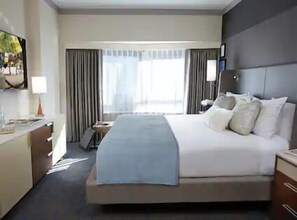 Hotellihuone, jossa on suuri sänky, työpöytä lampun kanssa, televisio ja ikkuna, jossa on verhot.