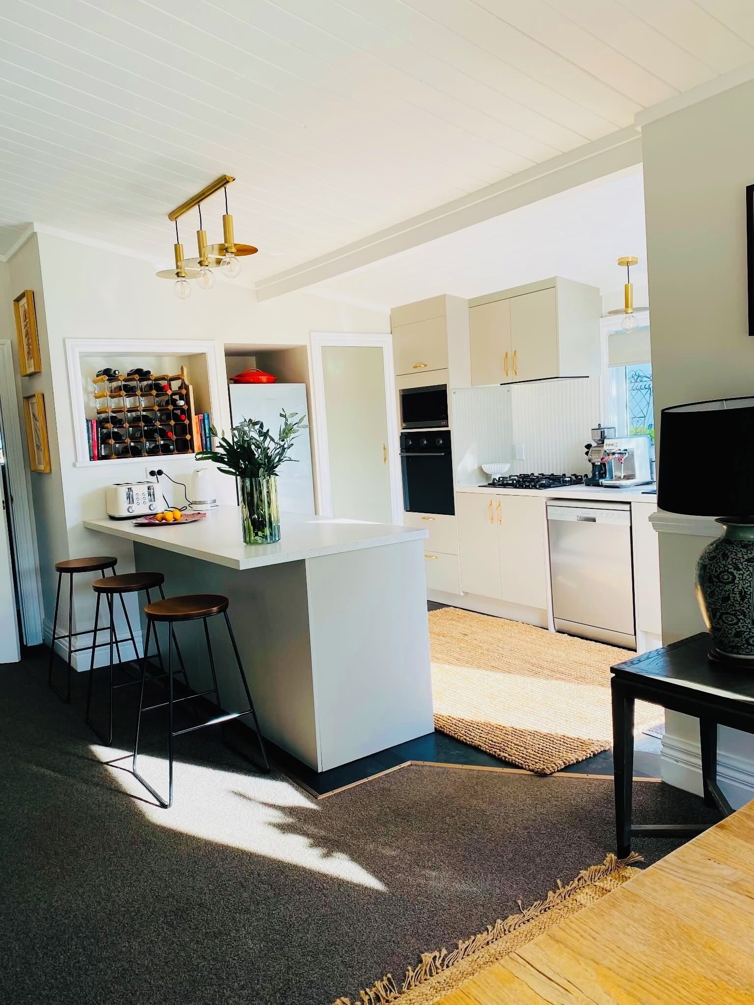 A modern kitchen with a central island, bar stools, a dining table, and a TV on a stand.