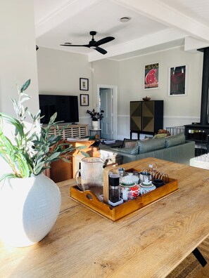 Ein Wohnzimmer mit Holztisch, weißer Vase mit grünen Blättern, Deckenventilator und Kaminofen in Schwarz.