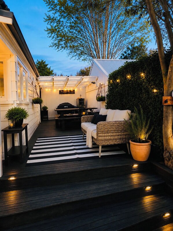 Une terrasse extérieure accueillante, avec un tapis rayé noir et blanc, un canapé en osier, une table à manger et un barbecue.