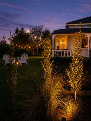 A house with a porch, two white chairs, and a lawn.