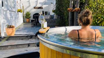 A hot tub in a wooden barrel with a view of a house and garden.