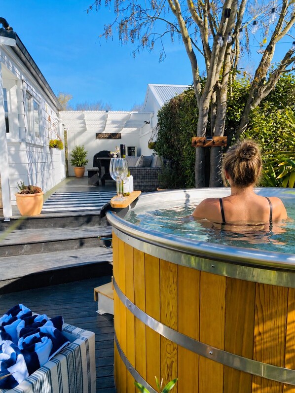 A hot tub in a wooden barrel with a view of a house and garden.
