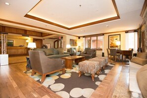 Uma sala de estar ampla com piso de madeira, um sofá grande, uma mesa de centro e um espaço de jantar com cadeiras e mesa.