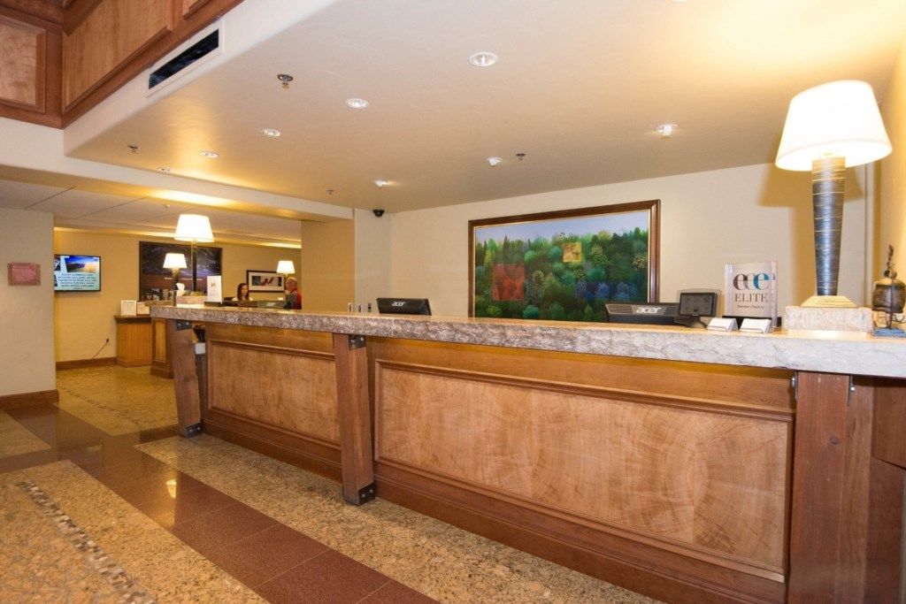 A hotel reception area with a marble counter, wooden paneling, a painting of a forest, and a sign that reads "Elite."