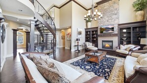A spacious living room with a fireplace, a staircase, and a large chandelier. - Luxury Aspen Woods Rental | 5 Bedrooms | 4.5 Bathrooms | 5,500+ SF (Calgary)