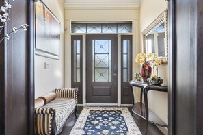A hallway with a double door, a bench, a rug, and a console table with a vase and flowers. - Luxury Aspen Woods Rental | 5 Bedrooms | 4.5 Bathrooms | 5,500+ SF (Calgary)