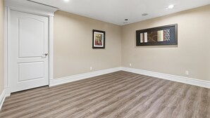 A room with a white door, beige walls, and a patterned wooden floor. There are two framed artworks on the walls. - Luxury Aspen Woods Rental | 5 Bedrooms | 4.5 Bathrooms | 5,500+ SF (Calgary)