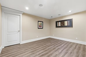 Ein Zimmer mit einer weißen Tür, beigen Wänden und einem Holzfußboden mit Muster. An den Wänden hängen zwei gerahmte Kunstwerke.