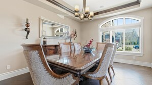 A dining room with a large wooden table, ornate chairs, a chandelier, and a large window with a view. - Luxury Aspen Woods Rental | 5 Bedrooms | 4.5 Bathrooms | 5,500+ SF (Calgary)