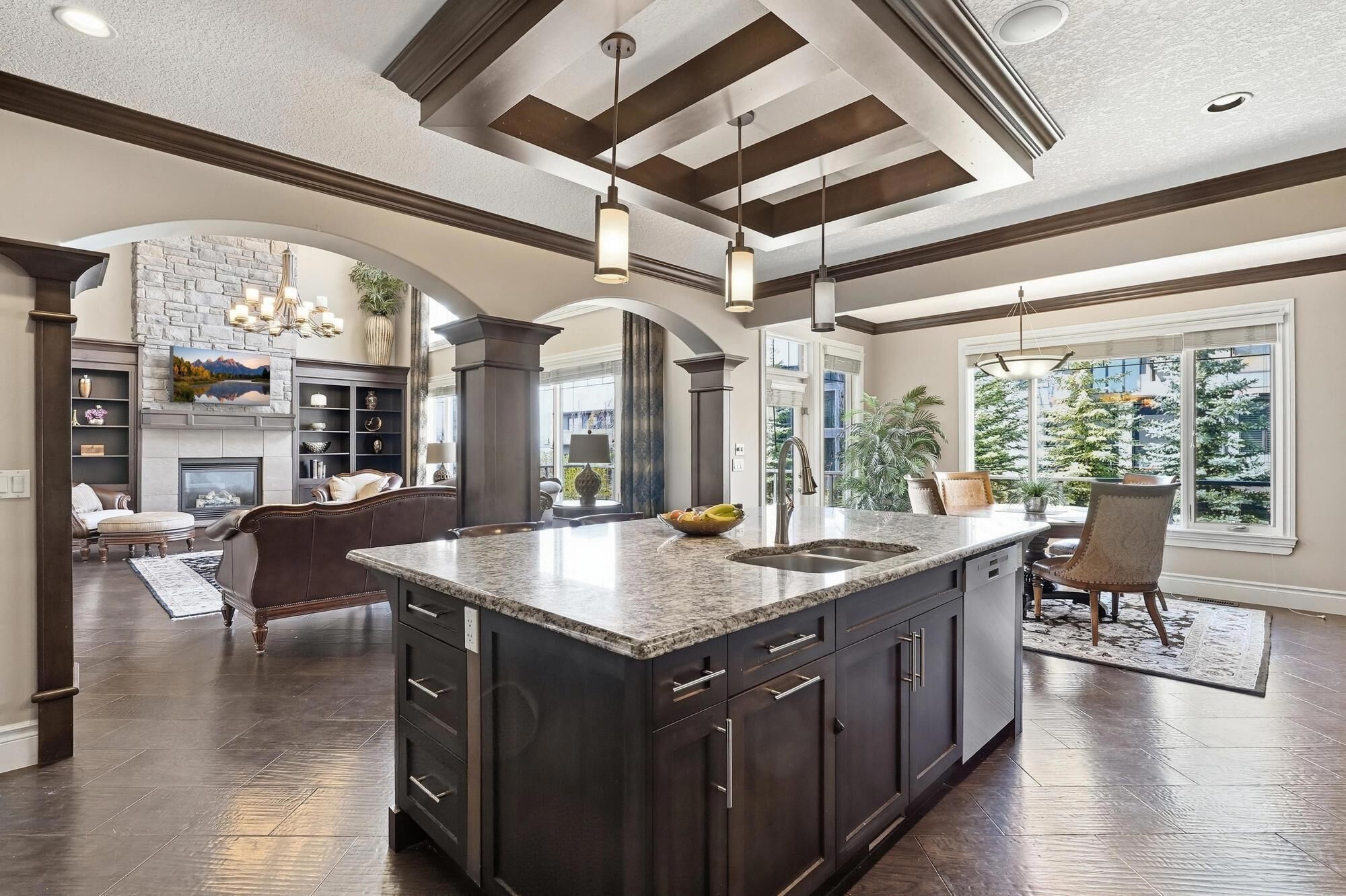 A spacious kitchen with a large island, dark cabinetry, and a view of a snowy landscape through large windows.