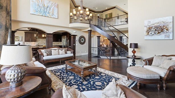 A spacious living area with a grand staircase, a chandelier, and a large painting. - Luxury Aspen Woods Rental | 5 Bedrooms | 4.5 Bathrooms | 5,500+ SF (Calgary)