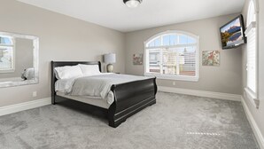 A bedroom with a bed, a window with blinds, a wall-mounted TV, and a ceiling light. - Luxury Aspen Woods Rental | 5 Bedrooms | 4.5 Bathrooms | 5,500+ SF (Calgary)