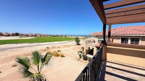 A residential area with a view of a golf course, a sandy beach, and a building with a red-tiled roof.